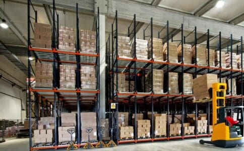 Warehouse interior with high shelves filled with boxes and a forklift in operation, showcasing an organized storage system.